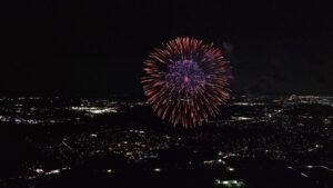 夜の市街地上空で打ち上げられる花火を上空から捉えた夜景の空撮イメージ